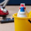 Red vacuum cleaner and plastic bucket with liquid detergents on beige carpet. Housekeeping concept